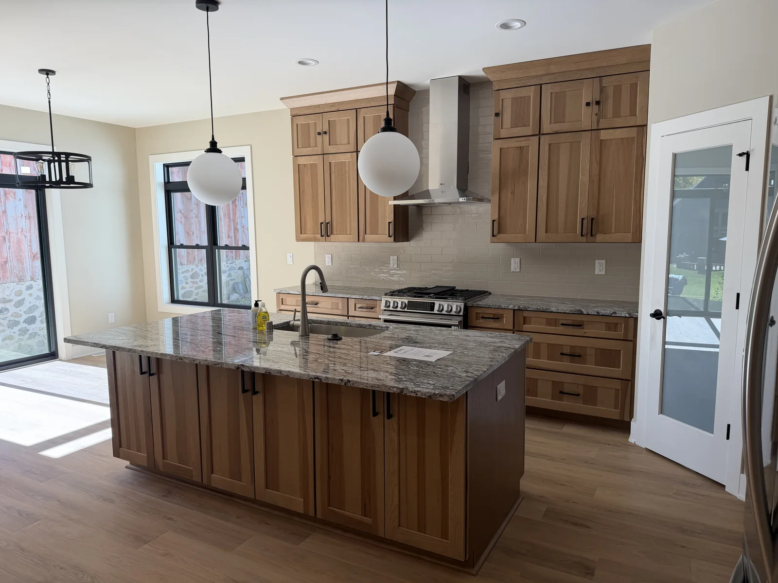 Newly built home kitchen with wood cabinetry, stone island and globe pendant lights