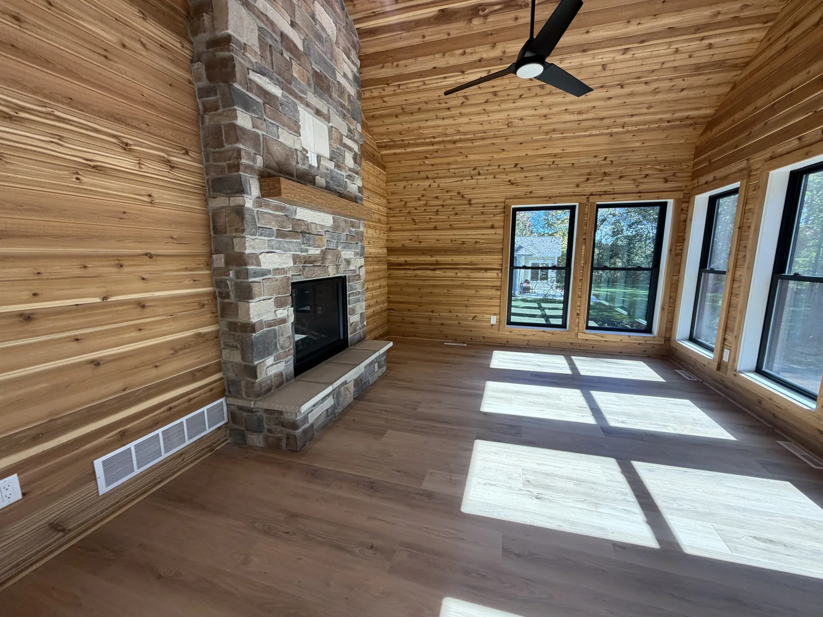 Wood-paneled room in a newly built home with a stone fireplace and black-framed windows