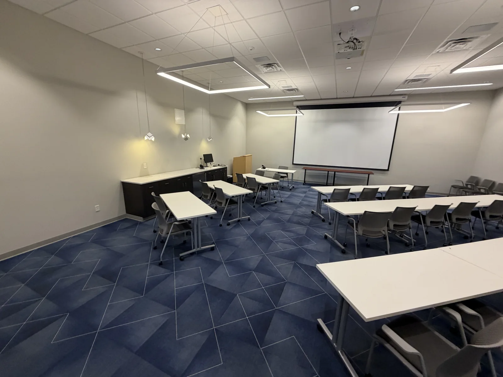 Meeting room with white tables, chairs and a projection screen